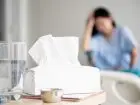 Zwolnienia lekaskie na COVID - kobieta trzymająca się za głowę, chora, chusteczki na stole