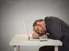 Mężczyzna śpiący na laptopie przy biurku