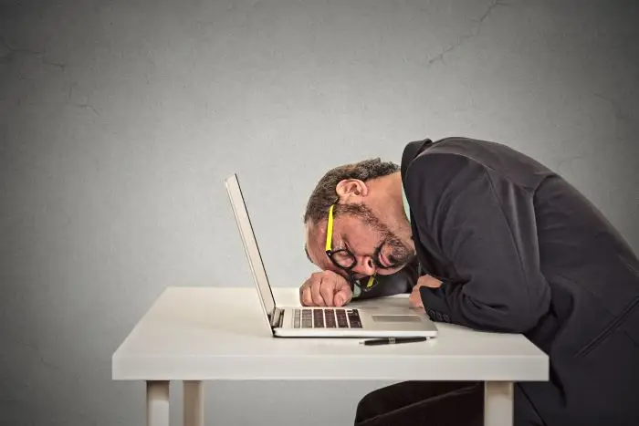 Mężczyzna śpiący na laptopie przy biurku