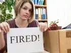 Status bezrobotnego - kobieta przy biurku trzymająca kartkę z napisem fired