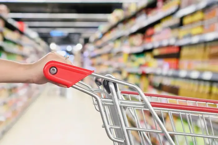 Kobieta w supermarkecie na zakupach, pchająca wózek zakupowy