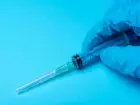 Szczepionka trzymana w dłoni w rękawiczce na niebieskim tle