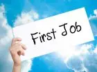 Napis "first job" na kartce trzymanej w dłoni na tle nieba