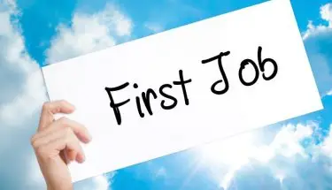 Napis "first job" na kartce trzymanej w dłoni na tle nieba