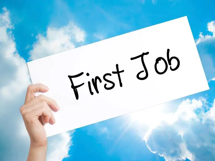 Napis "first job" na kartce trzymanej w dłoni na tle nieba