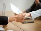 Dwie osoby podają sobie dłonie na tle umowy
