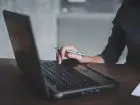 Kobieta pisząca na komputerze z długopisem w dłoni