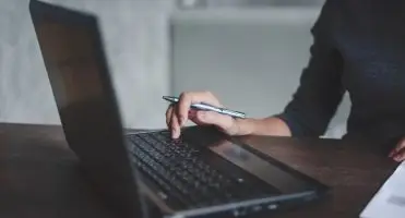 Kobieta pisząca na komputerze z długopisem w dłoni