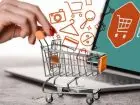 Miniaturowy wózek zakupowy pchany przez dłoń kobiety na tle ekranu laptopa