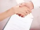 Dwie osoby podające sobie dłonie na tle dokumentów