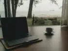 Laptop na biurku, obok kawa, za oknem morze