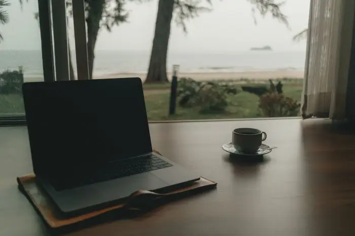 Laptop na biurku, obok kawa, za oknem morze