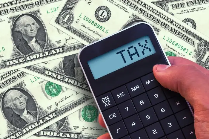 Napis tax na kalkulatorze trzymanym na tle dolarów