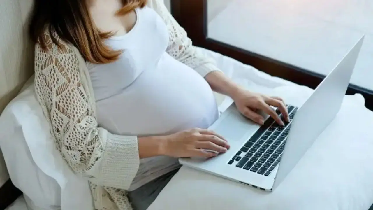 Kobieta w ciąży leżąca na łóżku z laptopem