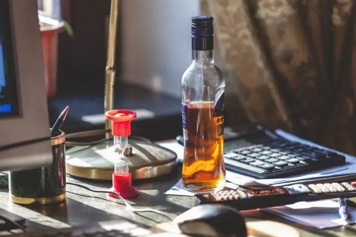 Butelka alkoholu postawiona na biurku, obok komputera