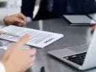 Umowa na biurku, obok laptop i tablet, zbliżenie na dłonie rozmówców