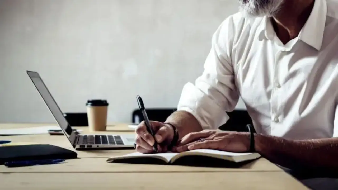 Elegancko ubrany mężczyzna piszący w notatniku i używający laptopa