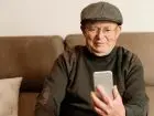 Podwyzki rent i emerytur 2025 - usmeichnięty emeryt na kanapie z telefonem w dłoni