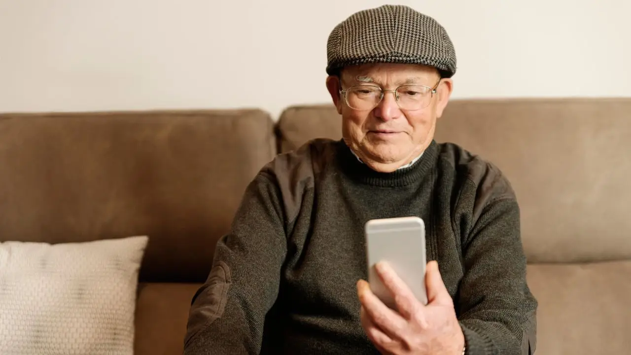 Podwyzki rent i emerytur 2025 - usmeichnięty emeryt na kanapie z telefonem w dłoni