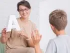 Logopeda - fajny logopeda pomaga chłopakowi w szarej koszuli poprawnie wymawiać słowa w białym pokoju