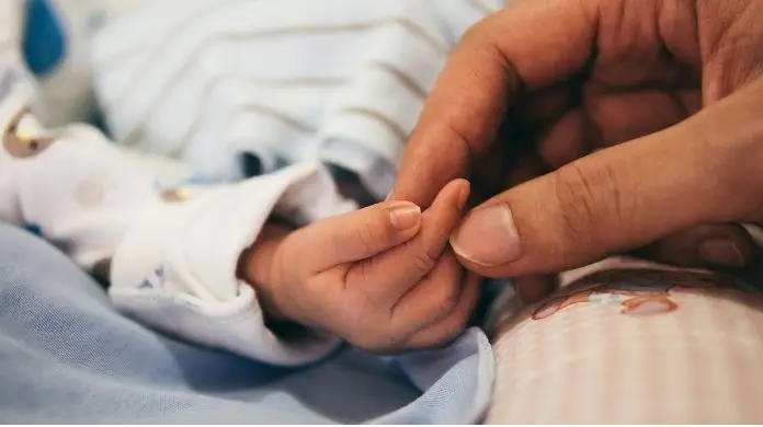 Zmiany w zasiłkach - dłoń matki trzymająca dłoń noworodka