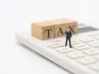 Napis TAX na kalkulatorze i miniaturowa figurka człowieka