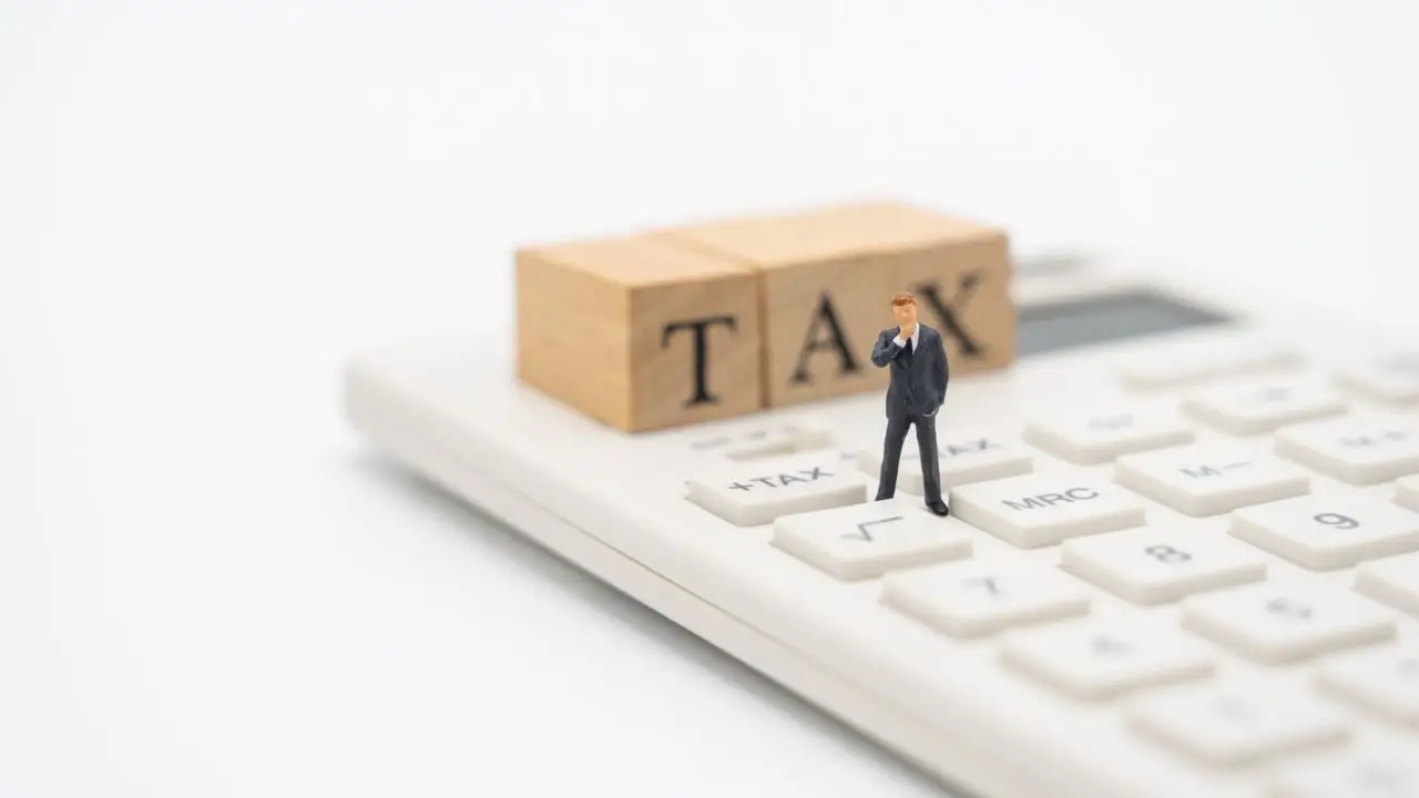 Napis TAX na kalkulatorze i miniaturowa figurka człowieka