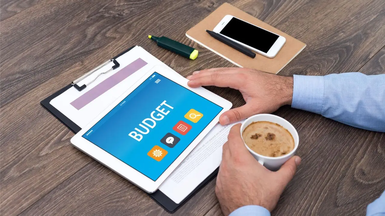 Budżetówka - napis budget na tablecie używanym przez mężczyznę pijącego kawę