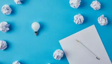 Biała kartka z długopisem i żarówką na niebieskim tle