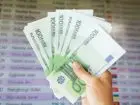 Banknoty w dłoni na tle tablicy z kursami walut