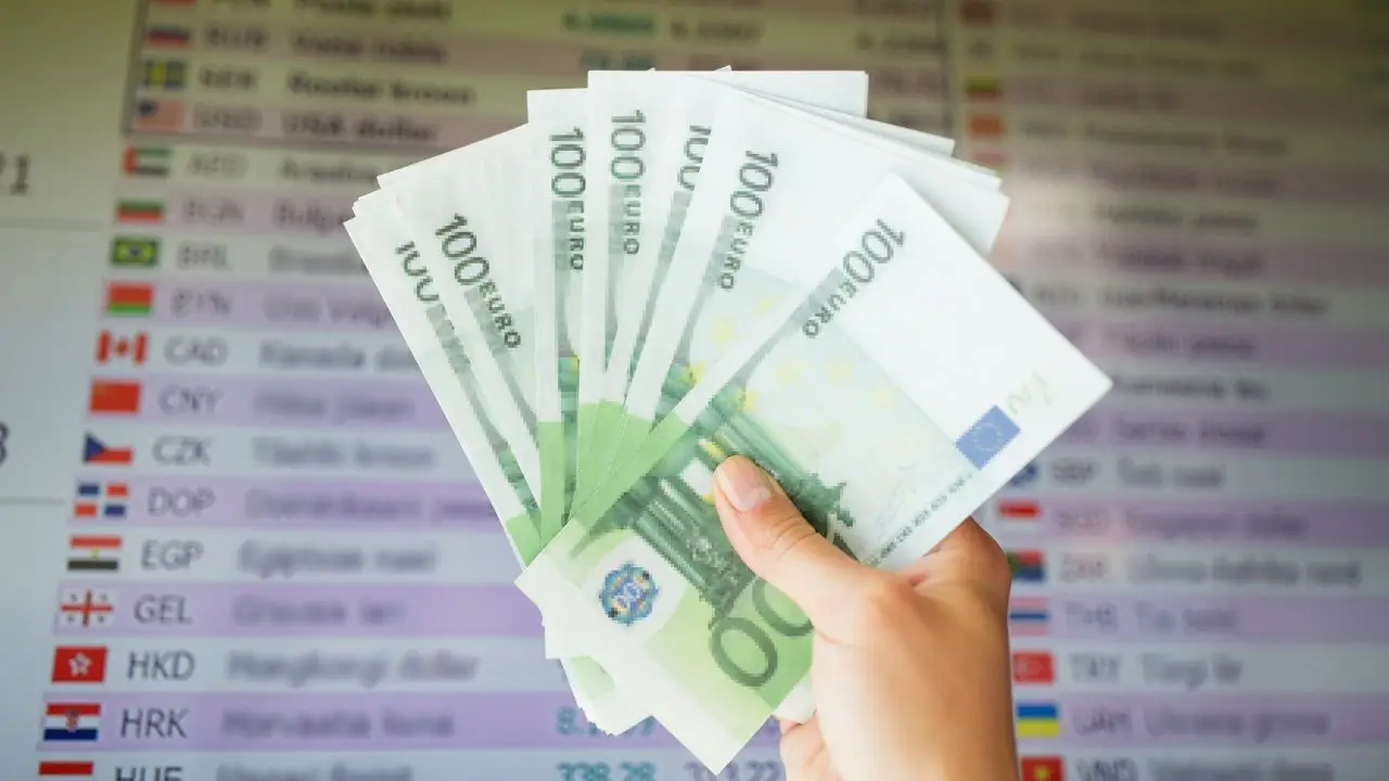 Banknoty w dłoni na tle tablicy z kursami walut