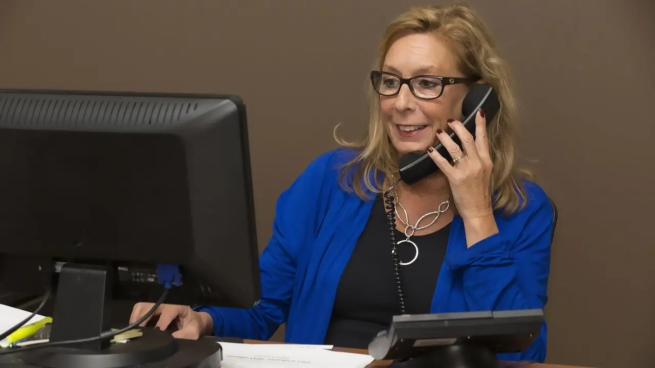 Rejestratorka medyczna - kobieta przy komputerze rozmawiająca przez telefon