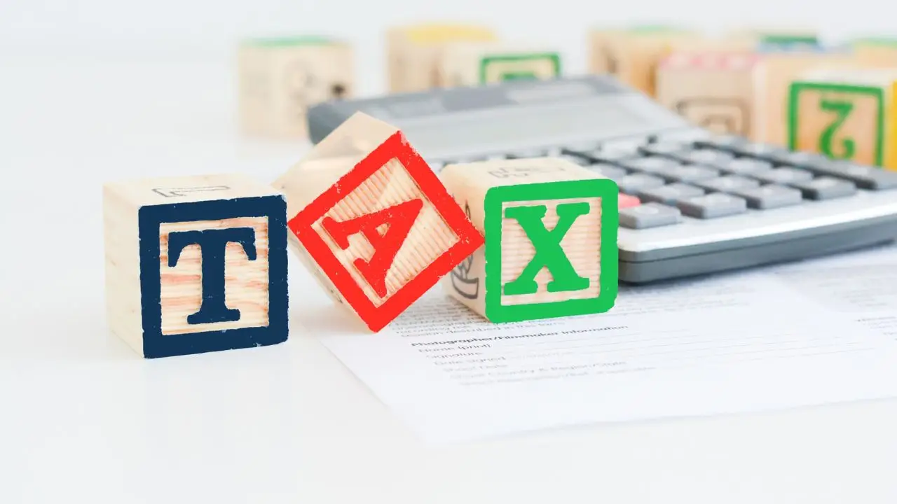 Obniżka podatku PIT do 12% - napis TAX ułożony z klocków i kalkulator w tle