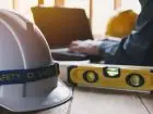 Jak zostać BHP-owcem - kas na tle pracownika budowy, obok poziomica