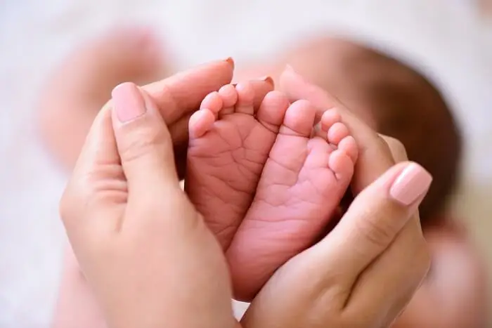 Położna-jak zostać położną? - położna trzyma małe nożki noworodka w swoich dłoniach