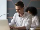 Stażysta - młody meżczyzna przy biurku pracuje na laptopie