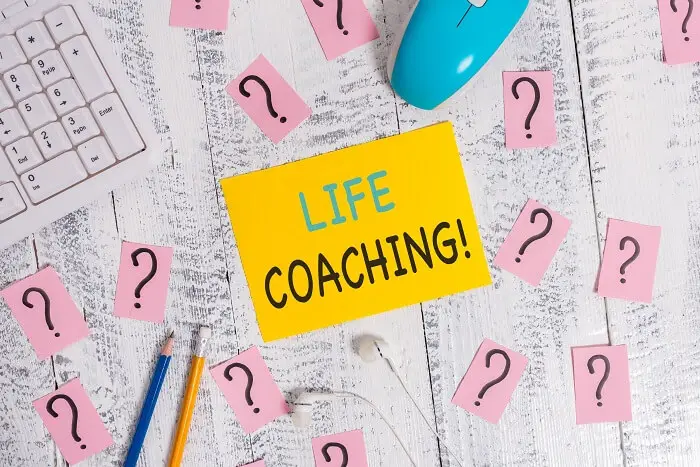 Jak zostać life coachem - karteczka z napisem "life coaching!" leżąca na biurku w otoczeniu znaków zapytania
