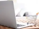 Praca Allegro - laptop, a obok miniaturowy wózek zakupowy