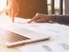 Zbliżenie na dłonie osób analizujących dokumenty przy laptopie