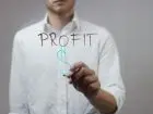 Po jakim czasie firma przynosi zyski - mężcyzna w koszuli rysujący na szybie symbol dolara i napis profit