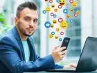 Meżczyzna korzystajacy z telefonu i laptopa, ikonki social mediów unoszące się w tle