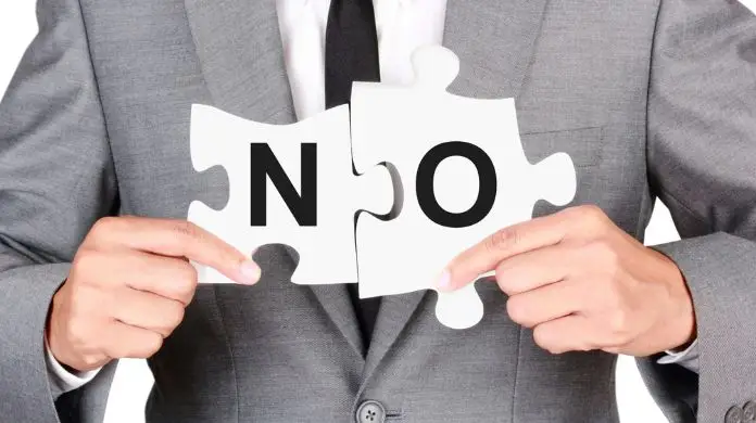 Jak kulturalnie odmówić awansu - pracownik w garniturze trzymający w dłoniach puzzle z napisem "NO", tzn. "nie" po angielsku