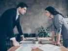 Konflikty w pracy - dwie osoby patrzące się na siebie przy biurku
