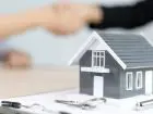 Wyższe ceny mieszkań a Bezpieczny Kredyt 2% - figurka domu postawiona na dokumentach