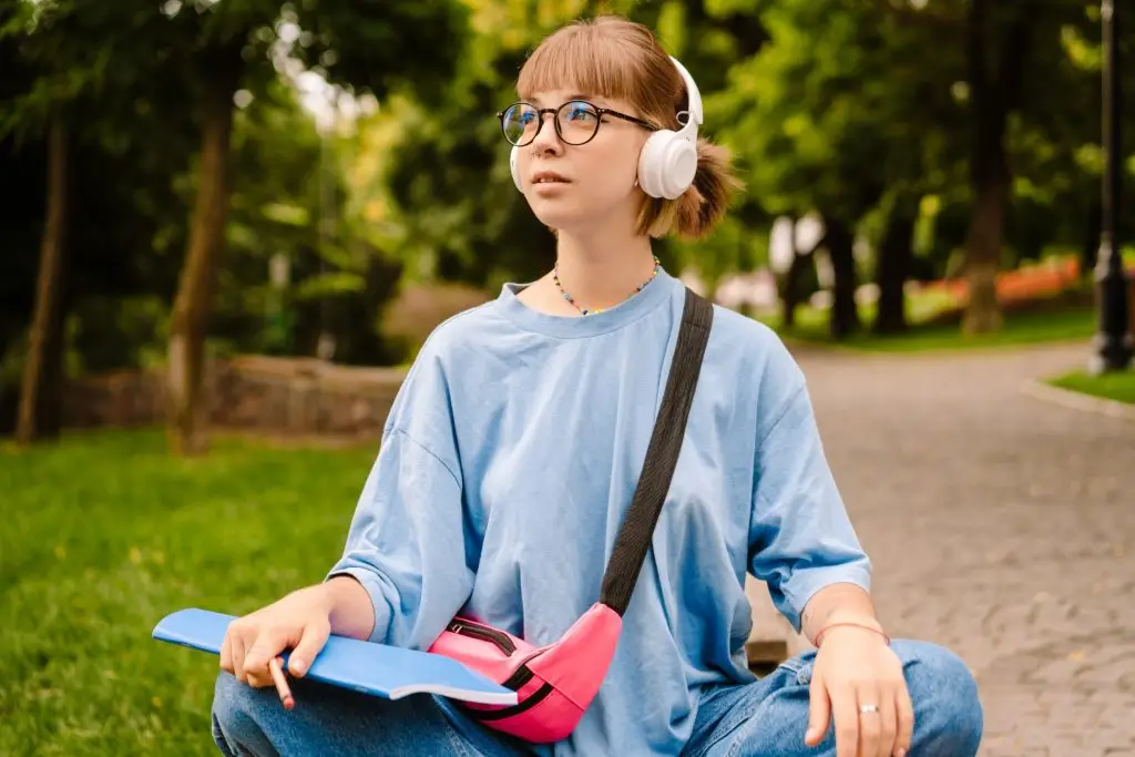 Jak uczyć się angielskiego za pomocą audiobooków - młoda kobieta siedząca w parku ze słuchawkami nałożonymi na uszy