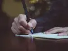 Zbliżenie na dłonie osoby piszącej w zeszycie