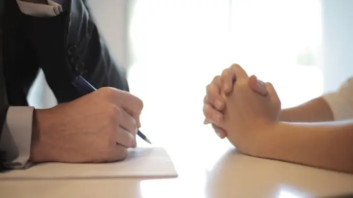 Testy behawioralne - dłonie dwóch osób siedzących na przeciwko siebie przy stole. Jedna osoba notuje
