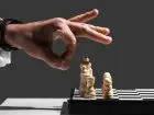 co to jest nieuczciwa konkurencja - dłoń uniesiona nad szachami, mężczyzna przymierzający się do zbicia figury