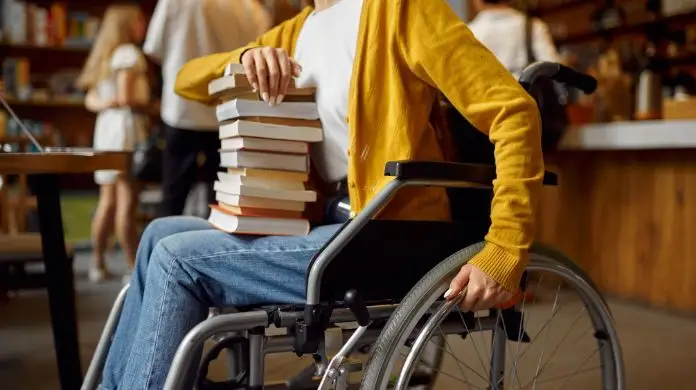 Osoba poruszająca się przy pomocy wózka, trzymająca książki na kolanach