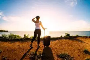 Migracja - kobieta z walizką patrzy na zachód słońca
